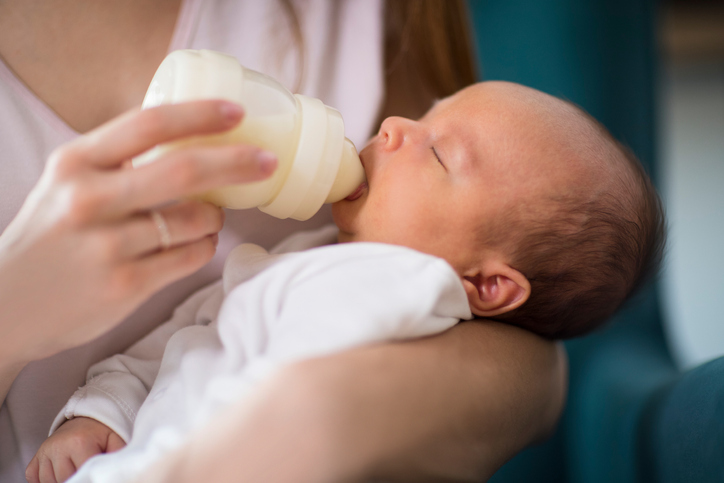 mother feeding baby formula milk in bottle